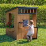 Caraway Cottage Light Brown Wooden Kids' Backyard Playhouse shown in an outdoor setting